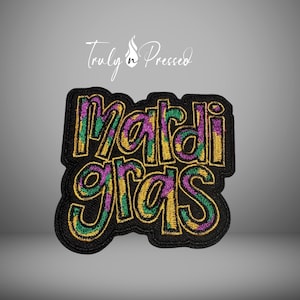 May include: Embroidered patch with the words "Mardi Gras" in gold, green, and purple on a black background. The patch has a black border and the text is in a stylized font. The patch is likely for clothing or accessories.