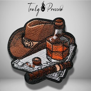 May include: An embroidered patch featuring a brown cowboy hat with a star emblem, a glass of amber liquid, a cigar, and a small round object resting on a white paper document. The text Truly Pressed is visible at the top of the design.