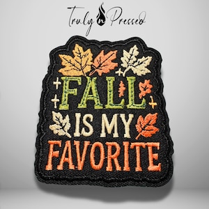 May include: A black embroidered patch featuring the text FALL IS MY FAVORITE in green, cream, and orange thread. The design is decorated with various autumn leaves in shades of yellow, orange, and cream, all set against a black fabric background.