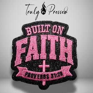 May include: A black glittery embroidered patch featuring the pink text BUILT ON FAITH and PROVERBS 31:28. The design includes a central pink cross symbol integrated into the lettering, all set against a dark, sparkling background with a black border.