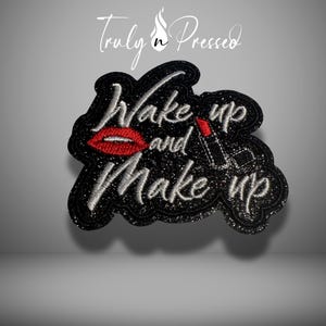 May include: Black glitter patch with the words "Wake up and Make up" in white script. The patch features a red lipstick and red lips. The brand name "Truly n Pressed" is at the top.