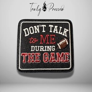 May include: A square embroidered patch with a black background and a white border. It features the white and red text "DON'T TALK to ME DURING THE GAME" and a small brown and white football graphic embroidered on the right side of the patch.