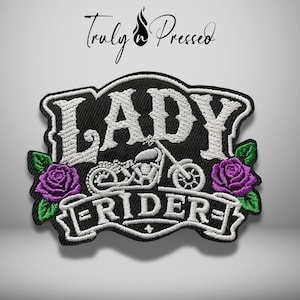 May include: A black embroidered patch featuring the white text LADY RIDER with a motorcycle graphic in the center. The design is flanked by two purple roses with green leaves on each side, all outlined in a thick black border on a white background.