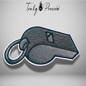 May include: An embroidered patch in the shape of a whistle, featuring dark gray thread with a white border. The design includes a circular ring attachment on the left side and a rectangular opening on the top. The text Truly Pressed is above.