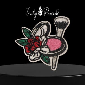 May include: Embroidered patch featuring a makeup brush and compact design with a red and white floral accent. The patch has a black outline and the text "Truly n' Pressed" in white script.