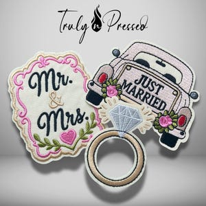 May include: Three embroidered patches featuring a cream-colored sign with pink trim and the text Mr. & Mrs., a light pink car with a Just Married license plate and floral accents, and a gold ring with a large diamond, all with black outlines.