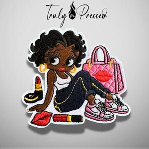 May include: An embroidered patch featuring a cartoon character with black hair, wearing a white tank top and dark pants, sitting next to a pink quilted handbag, two lipsticks, and a red lip icon. The text Truly Pressed is at the top.