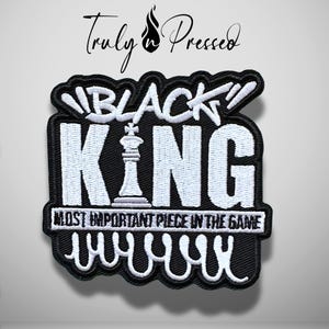May include: A black and white embroidered patch featuring the text "BLACK KING" with a chess king piece replacing the letter "I". Below, the text reads "MOST IMPORTANT PIECE IN THE GAME" with a decorative wavy line at the bottom edge.