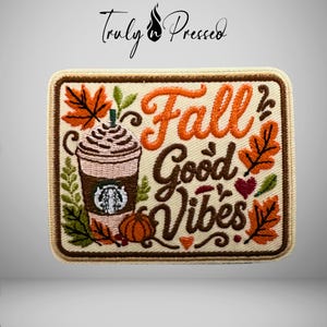 May include: A rectangular embroidered patch with a cream background and a brown border. It features a coffee cup with whipped cream, orange and brown autumn leaves, a small pumpkin, and the text Fall Good Vibes in orange and brown script.