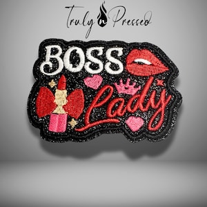 May include: Embroidered patch with the words "BOSS Lady" in white and red script. The patch features a red lipstick, pink hearts, a crown, and red lips on a black glitter background. The patch is a decorative accessory.