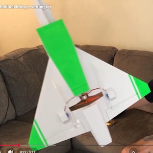 Peut inclure: Un mod&egrave;le d'avion blanc et vert avec le texte "Modified Mirage setting up". L'avion a un stabilisateur vertical vert et des accents verts sur les ailes. L'h&eacute;lice est visible.