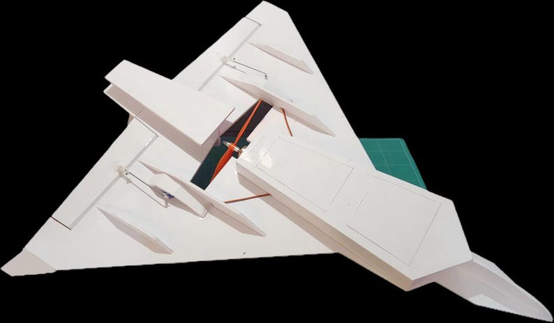 Peut inclure: Un mod&egrave;le r&eacute;duit d'avion blanc avec une aile delta. Le mod&egrave;le a un long corps rectangulaire et plusieurs petites ailes. L'h&eacute;lice est orange et noire. Le mod&egrave;le est sur un tapis de coupe vert.