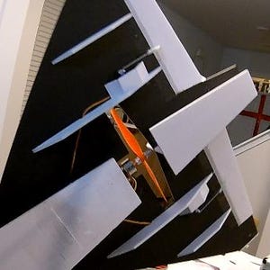 Peut inclure: Un mod&egrave;le d'avion partiellement assembl&eacute;, avec un corps noir et des ailes blanches. Le mod&egrave;le est &eacute;quip&eacute; d'une h&eacute;lice orange et de gouvernes. L'arri&egrave;re-plan r&eacute;v&egrave;le une pi&egrave;ce avec des meubles blancs et un drapeau.