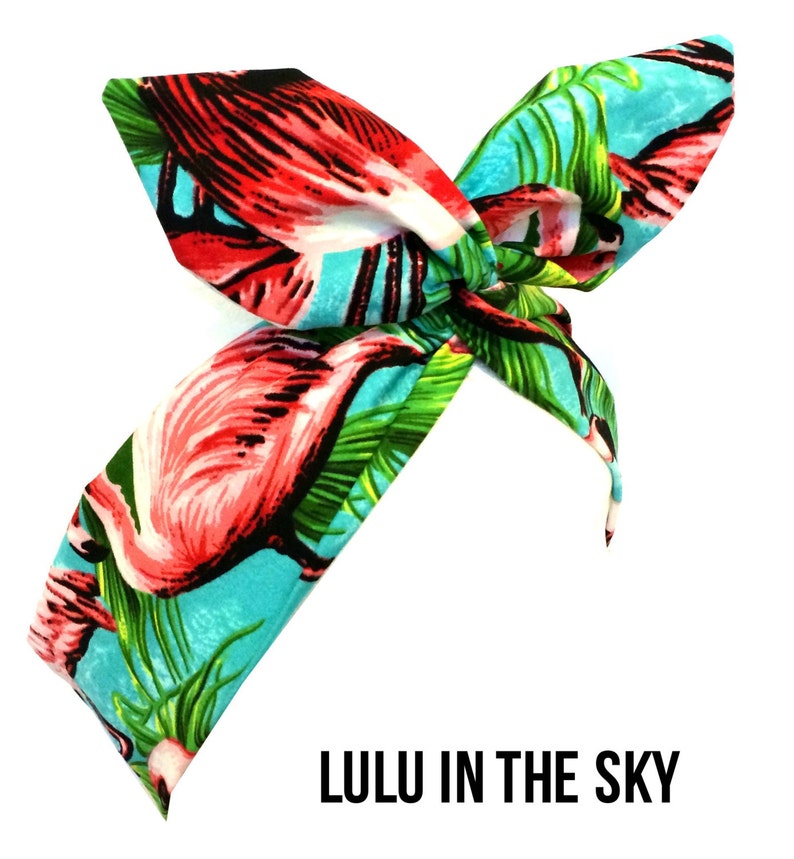 Puede incluir: Una diadema azul turquesa con estampado de flamenco rosa y hojas de palmera verdes. La diadema est&aacute; atada en un lazo y el texto "LULU IN THE SKY" est&aacute; impreso debajo de la diadema.