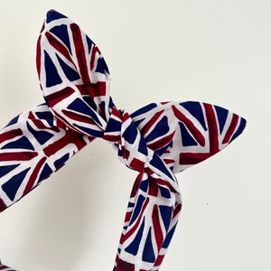 May include: A white, red, and blue fabric headband with a knotted design. The fabric features a pattern of the Union Jack flag.