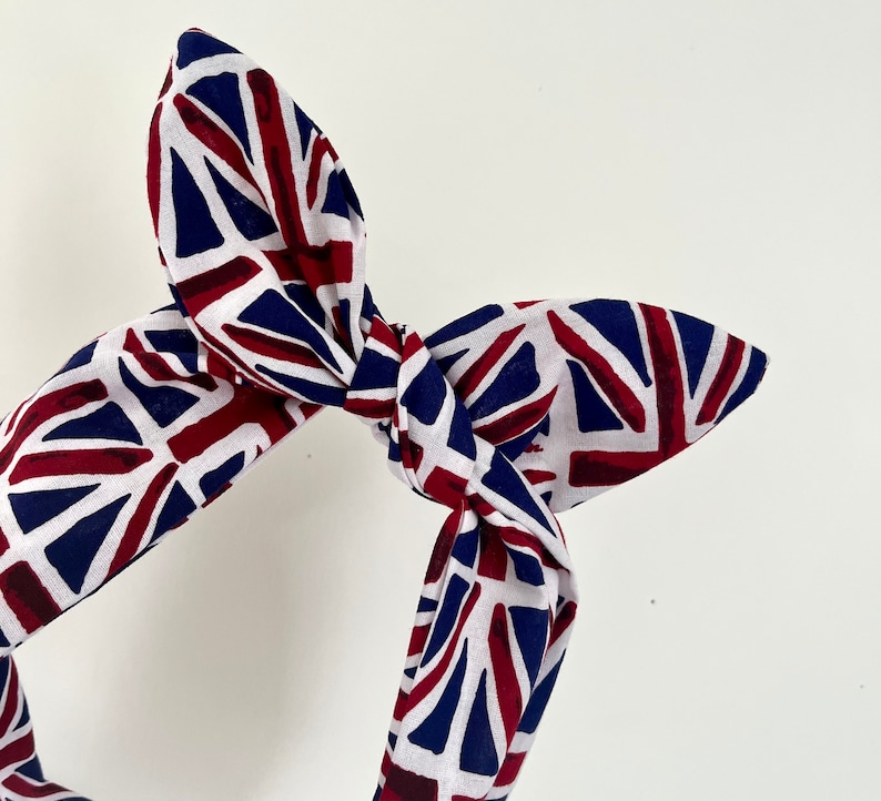May include: A white, red, and blue fabric headband with a knotted design. The fabric features a pattern of the Union Jack flag.