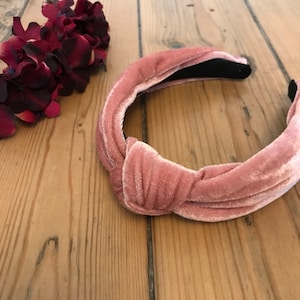 May include: A pink velvet knotted headband. The headband is made of soft, stretchy fabric and has a simple, elegant design.