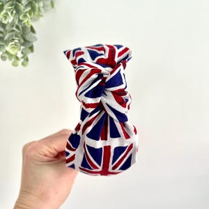 Puede incluir: Una diadema blanca anudada con un patr&oacute;n de Union Jack rojo, blanco y azul.