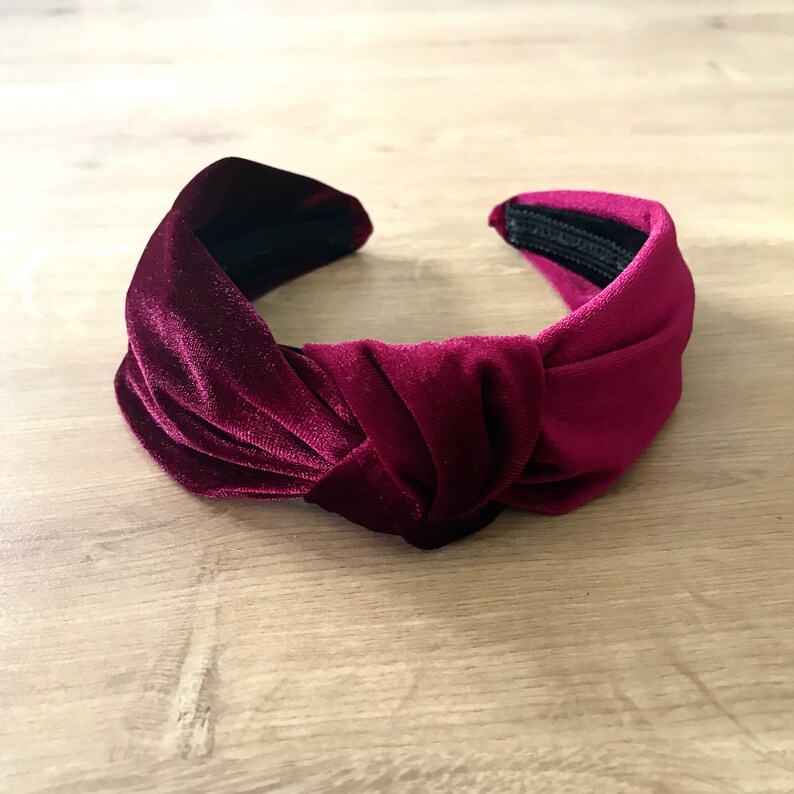 May include: A burgundy velvet knotted headband. The headband is made of soft, plush velvet and has a simple, elegant design.