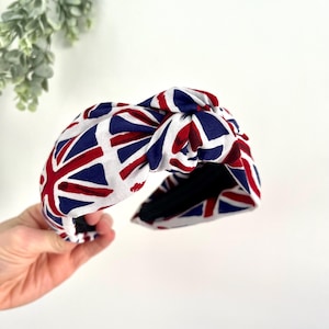Puede incluir: Una diadema blanca con un dise&ntilde;o anudado, con un patr&oacute;n de Union Jack rojo, blanco y azul.