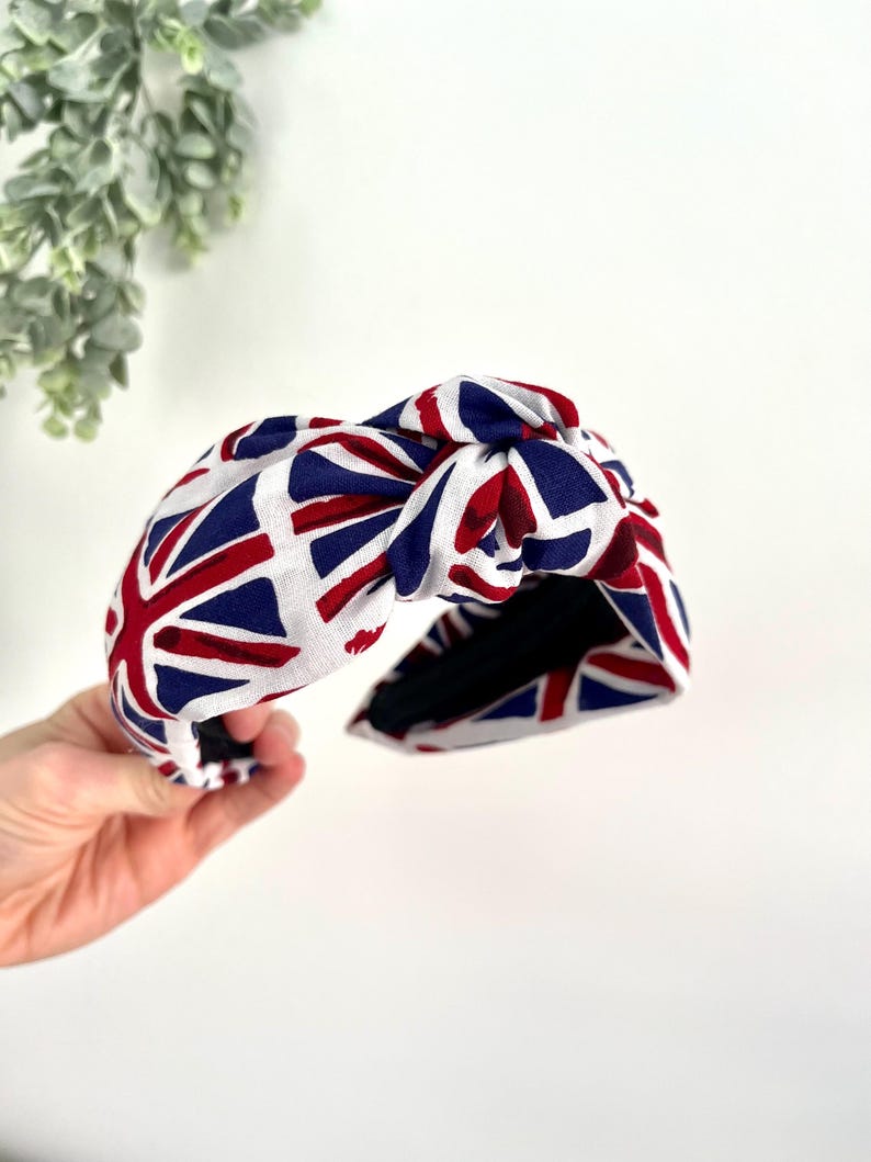 Puede incluir: Una diadema blanca con un dise&ntilde;o anudado, con un patr&oacute;n de Union Jack rojo, blanco y azul.