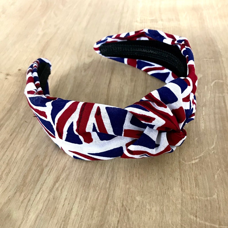 Puede incluir: Una diadema blanca, azul y roja con un dise&ntilde;o anudado. La diadema est&aacute; hecha de tela y tiene un patr&oacute;n de Union Jack.