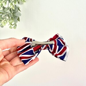 May include: A red, white, and blue bow with a Union Jack pattern. The bow is attached to a silver alligator clip.