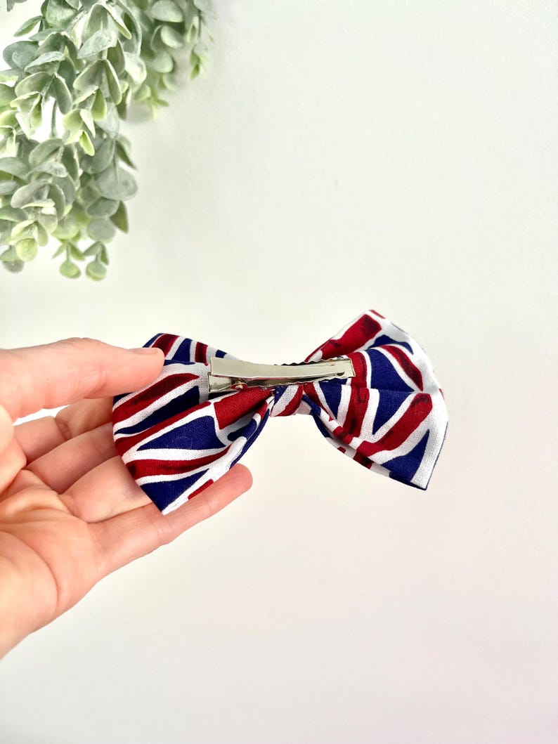 May include: A red, white, and blue bow with a Union Jack pattern. The bow is attached to a silver alligator clip.