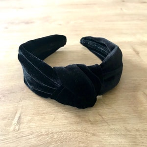 May include: A black velvet knotted headband. The headband is made of soft, plush velvet and has a simple, elegant design.
