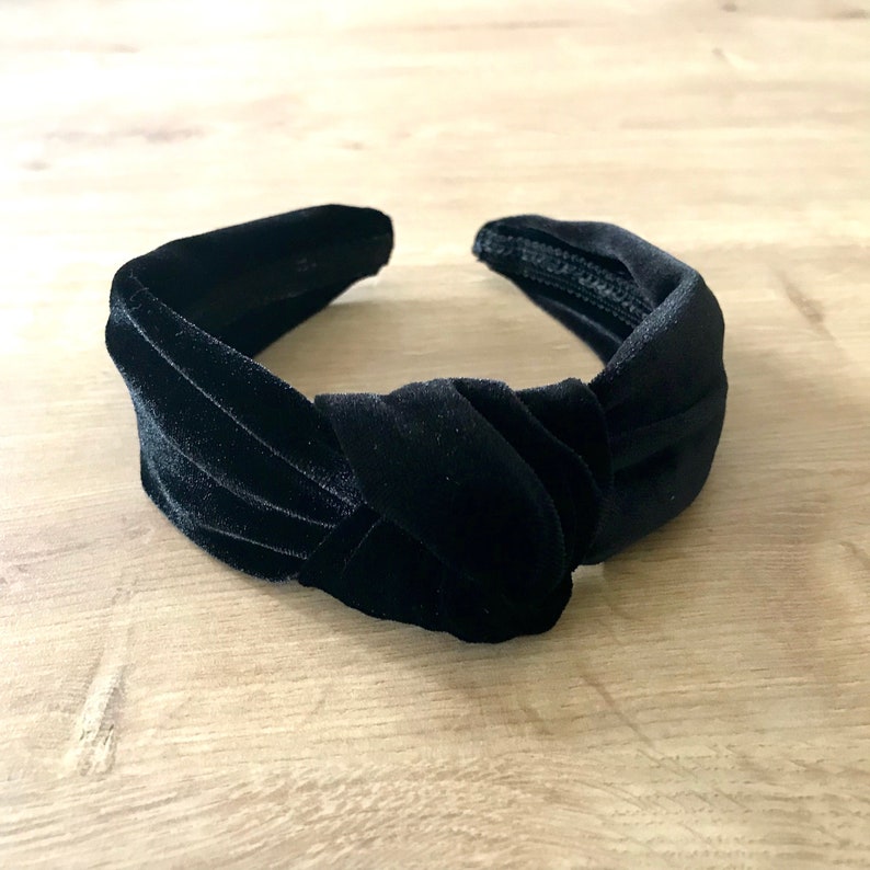 May include: A black velvet knotted headband. The headband is made of soft, plush velvet and has a simple, elegant design.