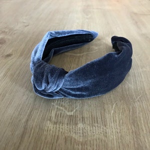 May include: A dark blue velvet knotted headband. The headband is made of a soft, stretchy material and has a simple, elegant design.