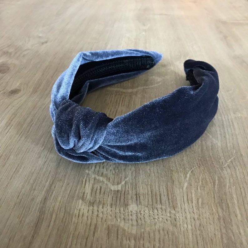 May include: A dark blue velvet knotted headband. The headband is made of a soft, stretchy material and has a simple, elegant design.