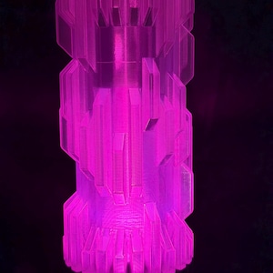 May include: A tall, cylindrical object with a geometric design, illuminated with a vibrant pink glow. The object has a layered structure with angular facets, creating a modern, artistic aesthetic. The base and top have a wider profile than the central section.