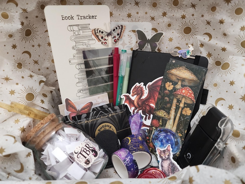 Pode incluir: Uma cole&ccedil;&atilde;o de artigos de papelaria incluindo um cart&atilde;o Book Tracker, um caderno preto, um frasco de vidro cheio de pap&eacute;is com a etiqueta TBR, dois rolos de fita washi estampada, um adesivo de drag&atilde;o, um marcador de cogumelos e um adesivo de gato.