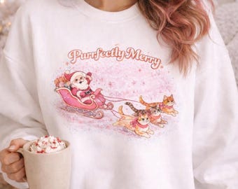 May include: White sweatshirt with a festive graphic. The design features Santa Claus in a pink sleigh pulled by three cats, with the text "Purrfectly Merry" above. A mug of whipped cream is held in the hand.