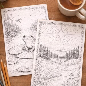 May include: Two black and white coloring pages with nature scenes, including a frog on a lily pad and a forest landscape, are displayed on a wooden surface. A cup of tea with a lemon slice and colored pencils are also present.