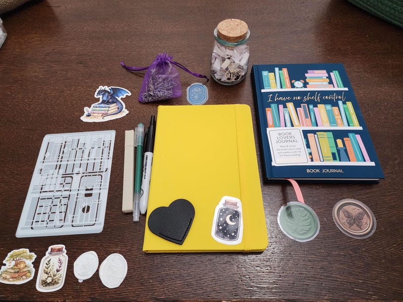 Puede incluir: Un conjunto de art&iacute;culos de papeler&iacute;a que incluye un cuaderno amarillo con pegatinas, un diario azul para lectores, un frasco de vidrio con tapa de corcho, una bolsa morada, tres bol&iacute;grafos, una plantilla y varias pegatinas decorativas.