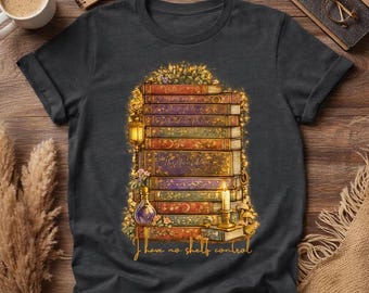 May include: Dark gray t-shirt featuring a stack of books with floral and lantern accents. The books have gold lettering and are surrounded by flowers. The text "I have no shelf control" is written in gold script.