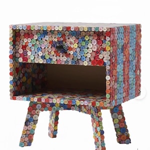 Könnte beinhalten: Ein farbenfroher Nachttisch, der mit einem Mosaik aus verschiedenen Knöpfen bedeckt ist. Die Knöpfe sind in einer Vielzahl von Farben gehalten, darunter Rot, Blau, Grün und Gelb. Der Nachttisch hat eine Schublade und ein offenes Regal. Die Beine sind gebogen.