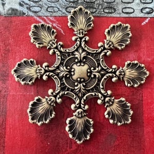 Peut inclure: Une décoration de flocon de neige en métal doré avec un design détaillé. Le flocon de neige a six pointes et chaque pointe a une forme de coquille.