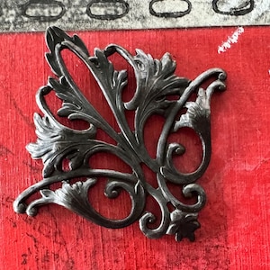 May include: A black metal decorative accent piece with a floral design. The piece is shaped like a leaf with intricate details and swirls.
