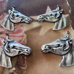 May include: Four silver-toned horse head pendants. Each pendant features a detailed horse head with a loop at the top for hanging. The pendants are arranged on a vintage-style background.