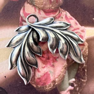 May include: A silver pendant in the shape of two stylized leaves. The leaves are detailed and have a textured surface.