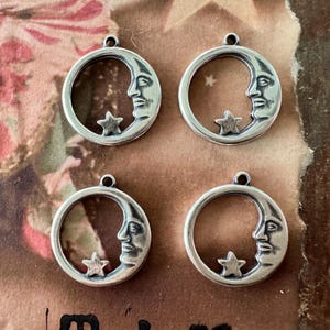 Könnte beinhalten: Vier silberfarbene Metall-Anhänger in Form einer Mondsichel mit einem Stern im Inneren. Jeder Anhänger zeigt ein stilisiertes Gesicht auf dem Mond.