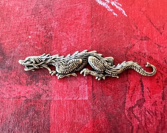 Op de afbeelding: Een zilverkleurig drakenbeeldje met gedetailleerde schubben en klauwen. De draak bevindt zich in een rennende houding met zijn kop naar de zijkant gedraaid.