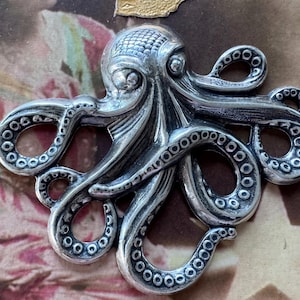K&ouml;nnte beinhalten: Ein detaillierter, silberfarbener Oktopus-Anh&auml;nger. Der Kopff&uuml;&szlig;er ist aufwendig gestaltet mit strukturierten Details auf seinem Kopf und Saugn&auml;pfen an seinen Tentakeln. Der Anh&auml;nger ist wahrscheinlich ein Schmuckst&uuml;ck oder ein dekoratives Element.