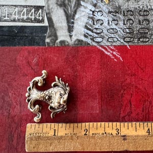 Puede incluir: Una figurita de pez de metal plateado con detalles intrincados. El pez tiene una cola rizada y una cara detallada. La figurita mide aproximadamente 5 cm de largo.