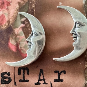 May include: Two silver crescent moon charms with a face sculpted on each. The moons are facing each other.