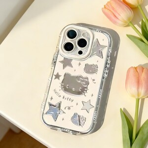 Może przedstawiać: Przezroczyste etui na telefon ze srebrnym wzorem Hello Kitty, gwiazdami i napisem "Lucky" wydrukowanym po bokach. Etui ma ochronny zderzak i wycięcie na aparat. Tło zawiera r&oacute;żowe tulipany.
