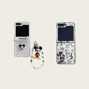 May include: Two phone cases with a Mickey Mouse theme. One case is white with black polka dots and a 3D Mickey Mouse head. The other case is white with black Mickey Mouse sketches. A Mickey Mouse charm is attached to the first case.